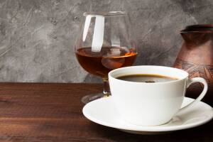 Coffee in white cup with cognac and clay cezve on wooden background. Copy space. Food background