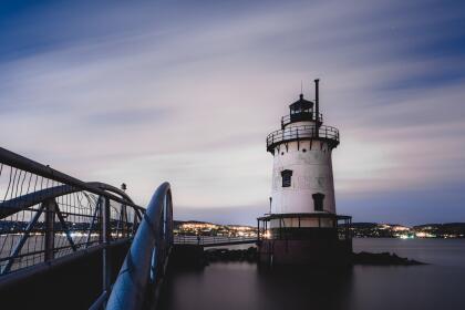 Tarrytown lighthouse in Sleepy Hollow, New York at night with calm water, fast moving clouds, and stars in the sky.