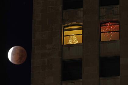 The earth's shadow covers the full moon during a partial lunar eclipse as it sets beyond an apartment building, Friday, Nov. 19, 2021, in downtown Kansas City, Mo. (AP Photo/Charlie Riedel)