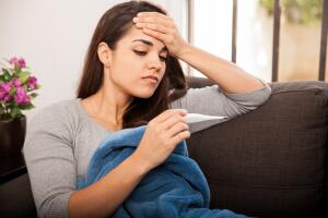 mujer con fiebre viendo el termómetro