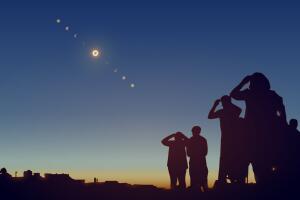 People are watching a solar eclipse in the sky with stars. 