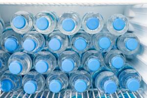 Rows of many transparent plastic bottles with drinking water supply in white refrigerator. Mineral water stack storage in fridge to drink on hot summer day. Healthcare and dehydration prevention