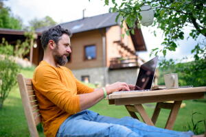 Side view of man with laptop working outdoors in garden, home office concept.