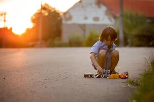 Cute sweet child, boy, playing with car toys on the street in village on sunset, summertime