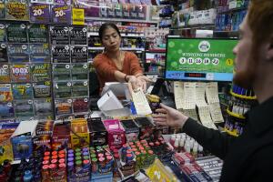 La gerente de una tienda de cigarrillos entrega un boleto de Powerball, que alcanzó la cifra de $ 1,400 millones para el sábado 7 de octubre de 2023.