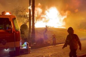 A firefighter passes by a fire engine in front of a burning house during wildfires in San Bernardino, California