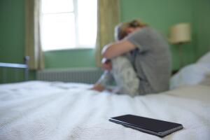 Young Woman In Bedroom Upset By Social Media Trolling And Cyber Bullying On Mobile Phone