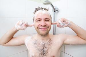 Youthful hairy guy washing in bathroom. A man enjoys washing his head and ears.