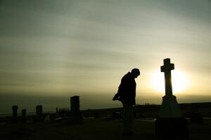 Silhouette of Caucasian Man Mourning at Graveyard