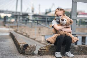 child in protective mask hugging teddy bear on street, air pollution concept