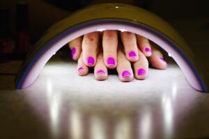 Two woman hand inside lamp for nails on table close up. UV lamp for drying nails with gel method. violet nails dried in the lamp