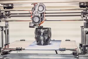 3D printer printing a model in the form of black skull close-up.