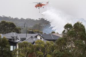 A Skycrane drops water on a bushfire in scrub behind houses in Bundoora, Melbourne