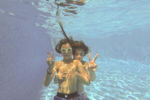 Two boys making v signs underwater in a swimming pool