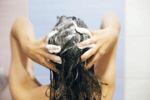 Young happy woman washing her hair with shampoo, hands with foam