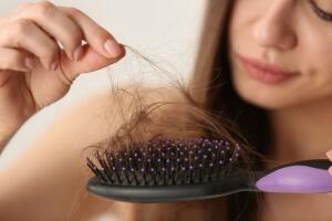 Woman untangling her hair from brush on light background, closeup 