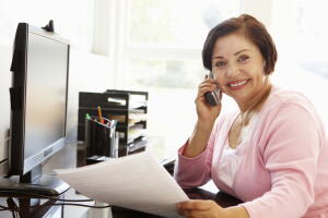 Senior lady in pink working at a computer desk using a phone
