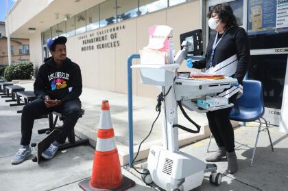 <b>California no se detiene.</b> Un trabajador del Departamento de Tránsito (DMV) de California atiende a los solicitantes de licencias fuera del edificio. A pesar del mandato estatal de permanecer en casa, esta oficina pública se ha mantenido abierta para atender las citas previas.