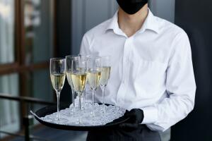 The waiter holds a tray with glasses of champagne. A waiter in a medical mask. Restaurant work during the coronavirus pandemic.