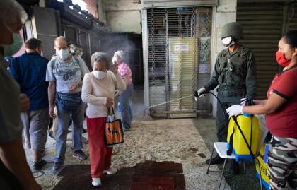 <b>Desinfección militar.</b> Un soldado rocía a los clientes de una tienda de alimentos con una solución desinfectante a base de cloro en Caracas, Venezuela, el 20 de marzo. En ese país se han registrado más de 70 casos de covid-19.