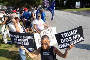 "Trump cavó su propia tumba" y "El sol brilla sobre las mentiras descaradas de Trump", se lee en los carteles que lleva en la mano este hombre que protesta contra el exmandatario, mientras seguidores de Trump lo esperan a las afueras de la cárcel de Fulton, en Atlanta.