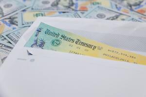 Stack of 100 dollar bills with coronavirus stimulus payment check to show the virus payment to Americans. Concept IRS tax refund or coronavirus stimulus payments. Global pandemic Covid 19 lock down