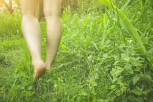Young woman walks barefoot on grass in meadow.
