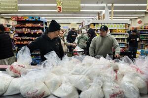 Alex Díaz, a la izquierda, toma una bolsa de malas para hacer tamales, mientras otros coladores esperan en fila en el mercado Amapola en Downey, California el martes 23 de diciembre 
