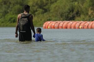 Migrantes pasan junto a grandes boyas de la barrera fronteriza flotante en el Río Grande en agosto de 2023, en Eagle Pass, Texas. 