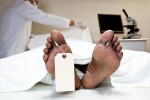 Mortician, coroner covering dead body in morgue. Feet, toe tag.