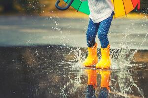 Feet of  child in yellow rubber boots jumping over  puddle in rain