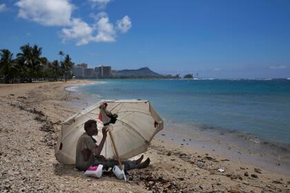 FILE - In this Aug. 27, 2015, file photo, a homeless man drinks water while sitting on the beach at Ala Moana Beach Park located near Waikiki in Honolulu, Hawaii. Hawaii is exploring setting up "safe zones" for homeless people to camp, one of an array of offbeat solutions to its homelessness crisis which ranks worst in the nation. (AP Photo/Jae C. Hong, File)