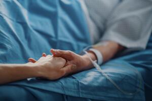 Hospital Ward: Senior Woman Resting in a bed with Finger Heart Rate Monitor, Caring Family Member Holds Her Fragile Hand, Support and Comforting. Focus on the Hands.