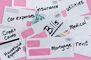 United States stimulus check issued in response to COVID-19 pandemic is almost completely covered by whites envelopes containing past due bills on pink paper with pink background and copy space.