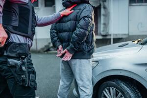 Police officer arresting a young gangster by the car