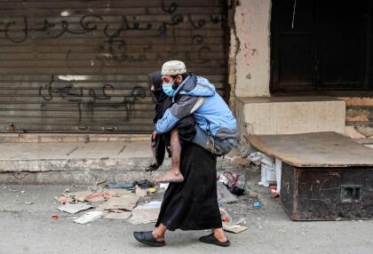 <b>Refugiados protegidos.</b> Una mujer lleva en su espalda a un hombre con una máscara contra el coronavirus en un campo de refugiados palestinos al sur de Beirut, Líbano. 22 de marzo.