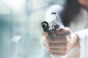 Woman pointing a gun at the target on blur background, criminal with gun, selective focus on front gun.