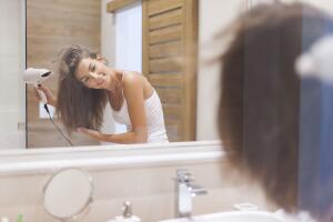 Happy woman drying her hair in bathroom. Photo taken through glass
