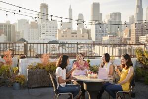 Female Friends Celebrating Birthday On Rooftop Terrace With City Skyline In Background