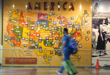 A traveler wears a face covering while pulling a carry-on bag past a map of America to reach the queue for the north security checkpoint in the main terminal of Denver International Airport Tuesday, Aug. 24, 2021, in Denver. (AP Photo/David Zalubowski)