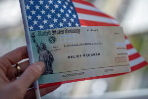 COVID-19 economic Stimulus check on blurred USA flag background. Relief program concept.
