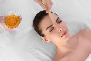Beautician depilating young woman's face with wax in spa center 